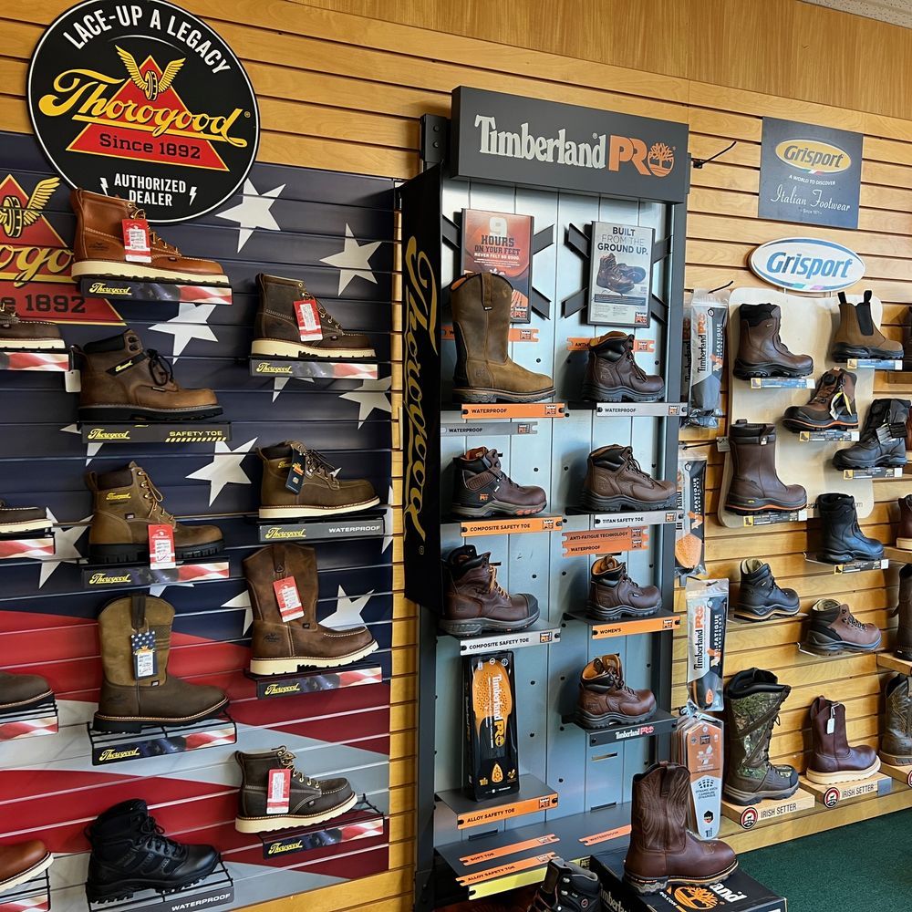 Display of work boots and safety shoes on wooden retail shelves with Timberland and other brand logos.