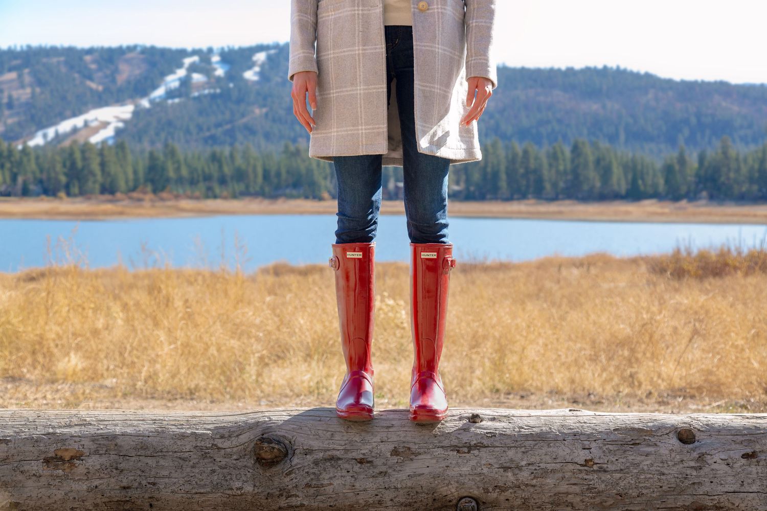 Red rain boots stand out against a golden autumn field with mountains and a lake in the background.