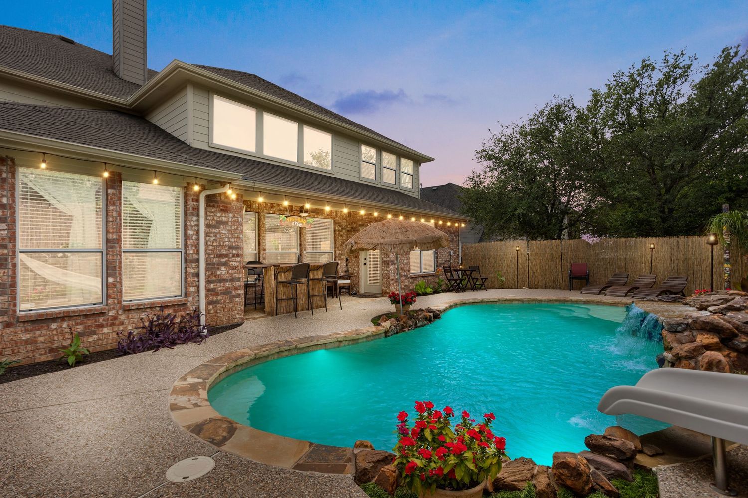 Luxury backyard pool with curved design surrounded by stone landscaping and modern outdoor lighting at twilight.