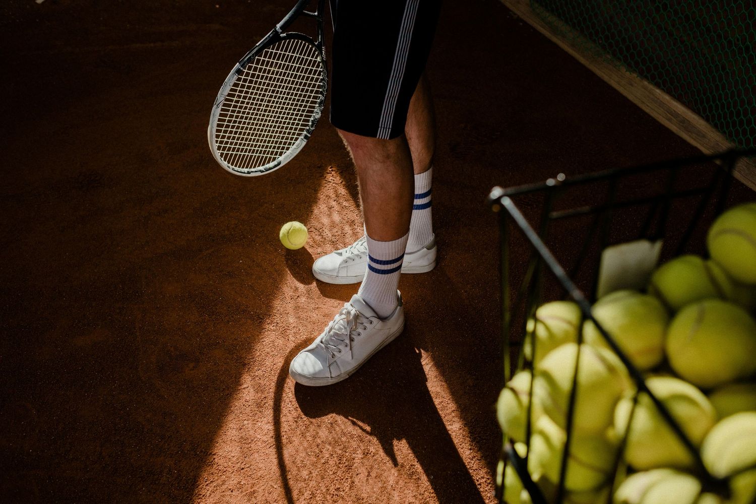 Tennis player wearing white socks picks up tennis ball from court surface in dramatic lighting.