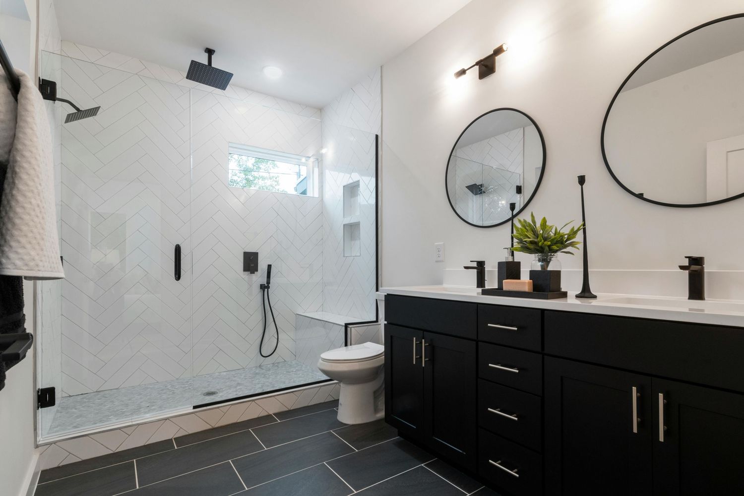 Modern black and white bathroom interior with double vanity, round mirrors, and sleek pendant lighting.
