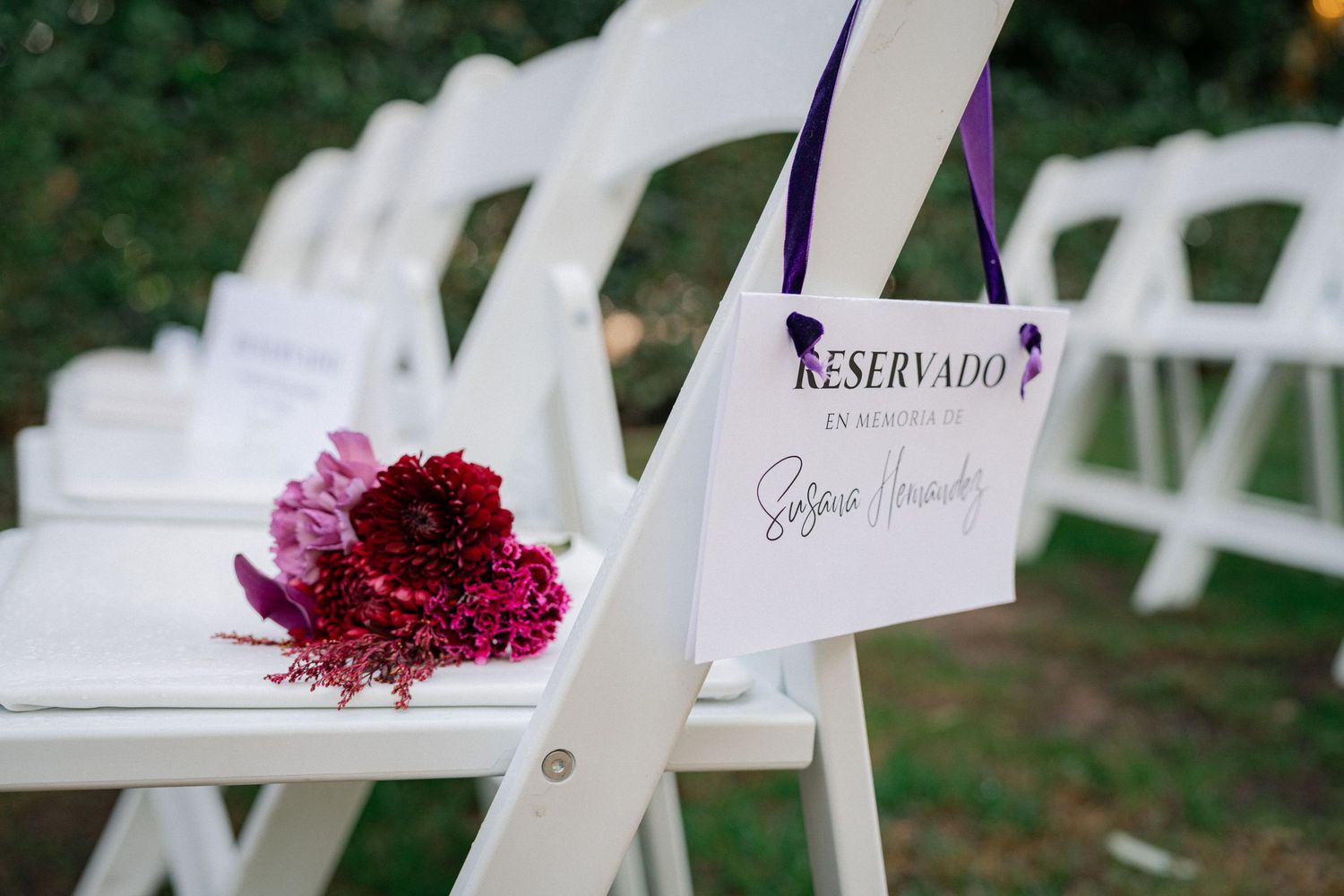 Decorative burgundy flower petals arranged on white folding chairs for an outdoor wedding ceremony.