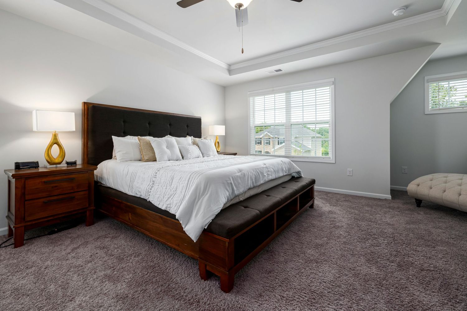 A modern master bedroom with grey carpet, white walls, and a dark wood bed frame in a spacious attic-style setting.