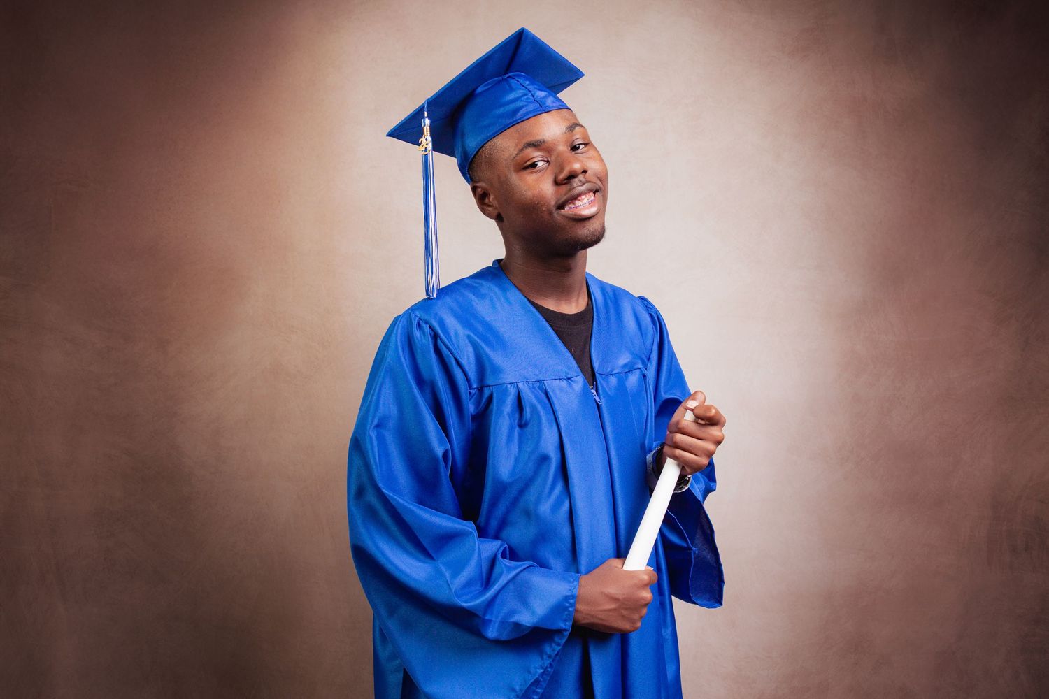 Graduate in bright blue cap and gown smiles joyfully while posing for celebratory graduation photos.