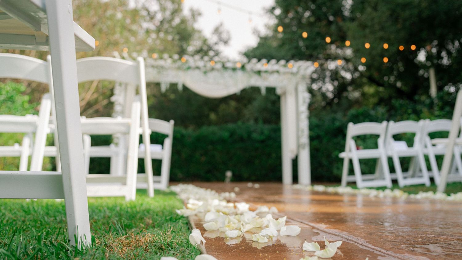White chairs arranged for an outdoor wedding ceremony with floral decorations and a rustic wooden arch.