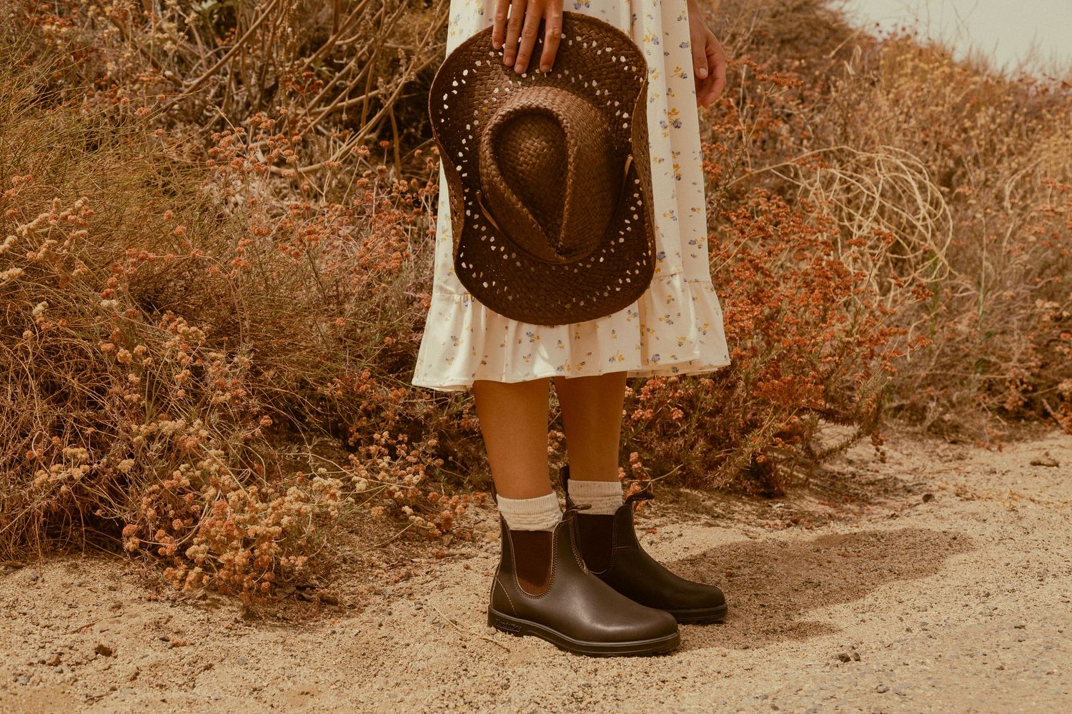 A vintage-inspired fashion photo showing brown leather boots, white socks, and a flowy dress with a cowboy hat.