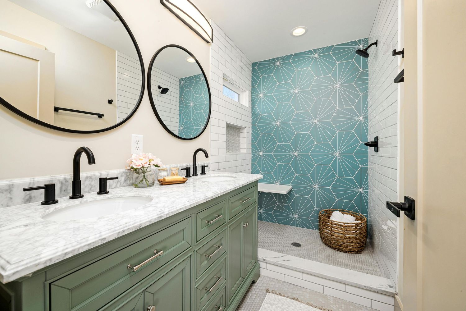 Modern bathroom renovation features sage green vanity with black hardware against turquoise geometric wallpaper.