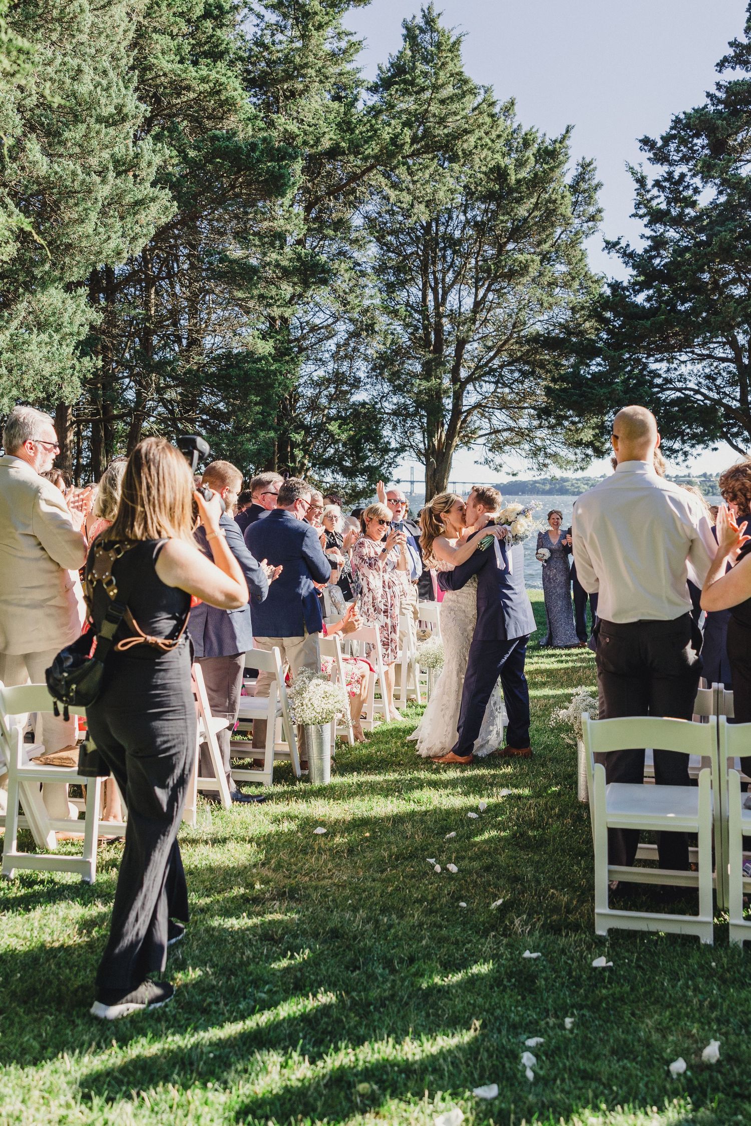 Outdoor wedding ceremony with guests standing and clapping in a pine forest setting. RI engagement photographer, Newport engagement photos,