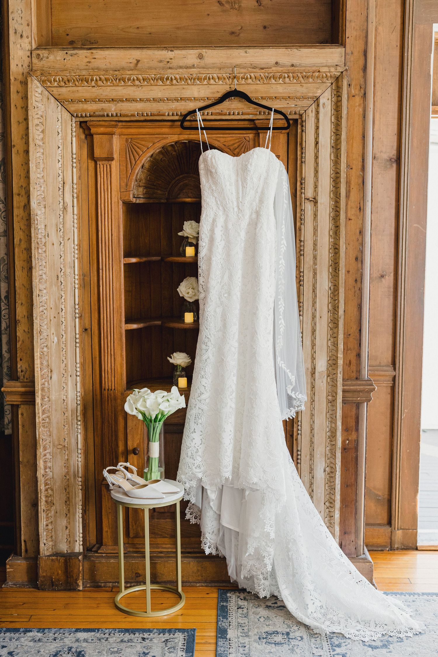 Multiple elegant white wedding dresses displayed on hangers in a rustic wooden room with ornate wall panels.