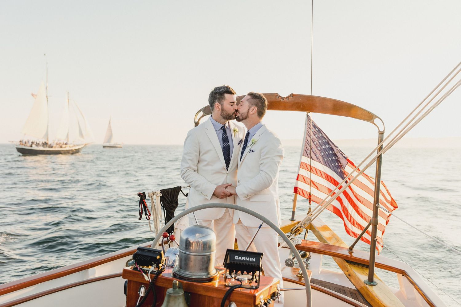 Romantic couple sailing together on a vintage wooden sailboat at sunset with American flag waving in the breeze.