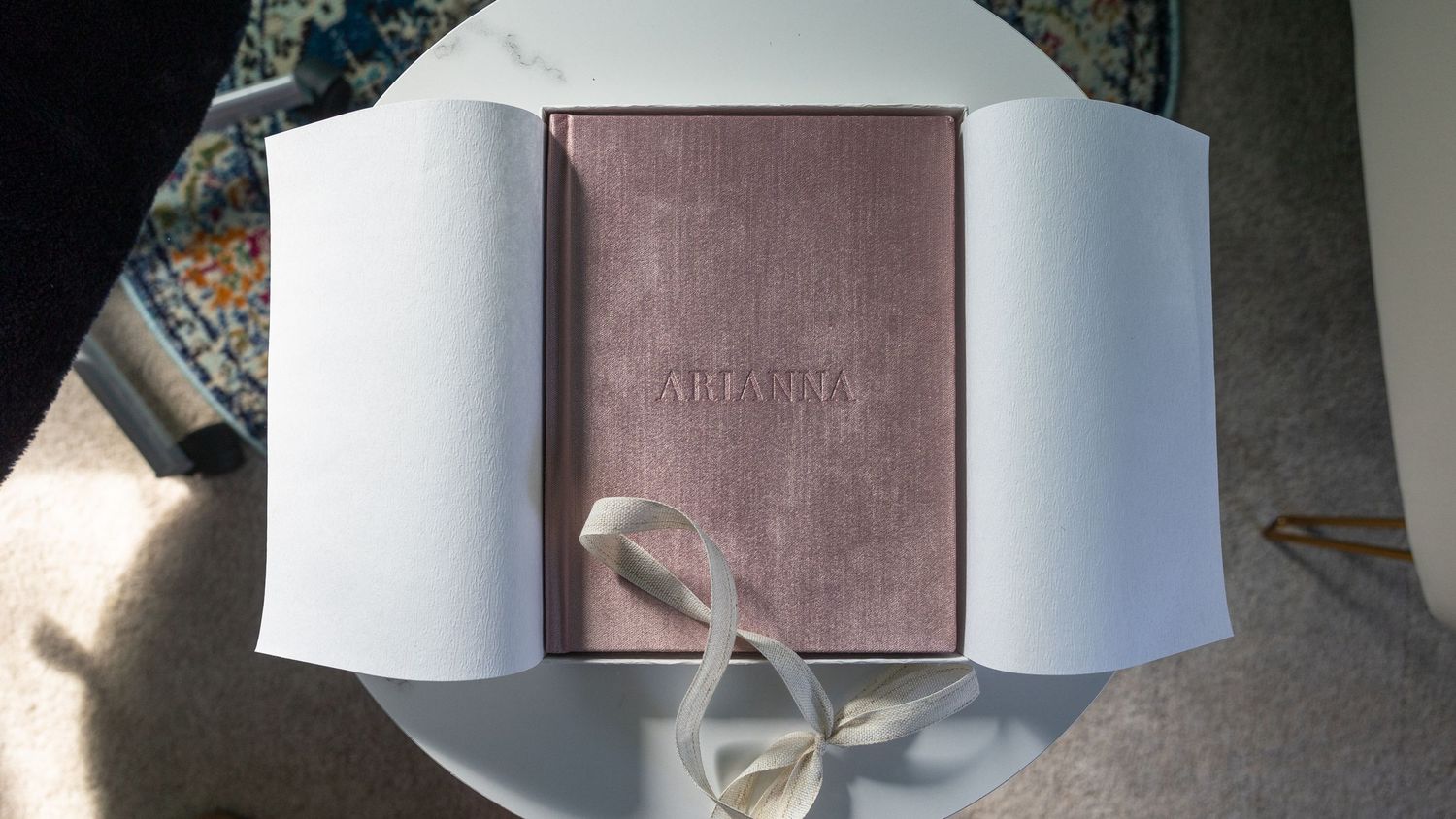 An elegant pink book nestled in white packaging with a delicate ribbon tie.