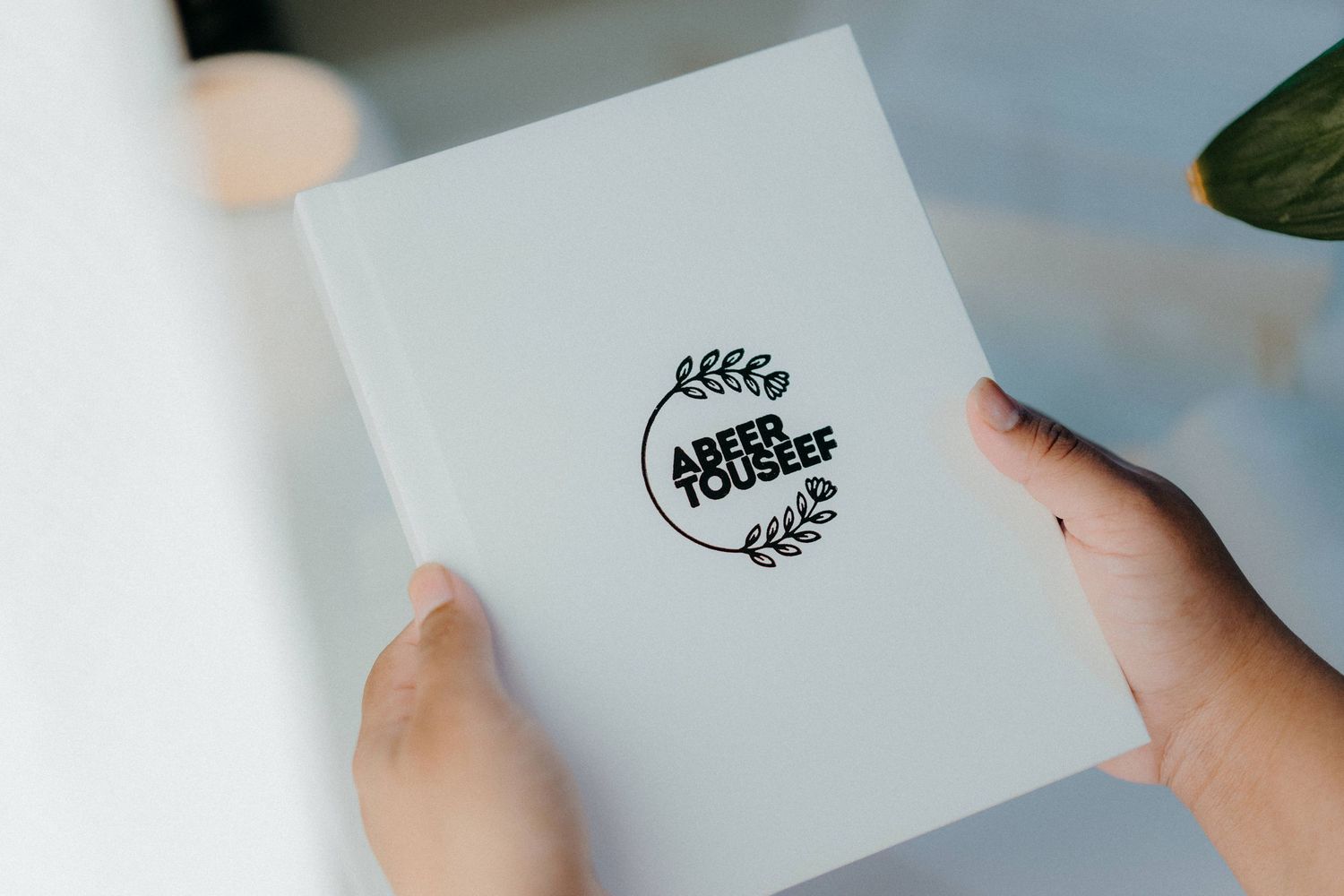 Hands holding a white wedding invitation card with a black circular floral logo design.