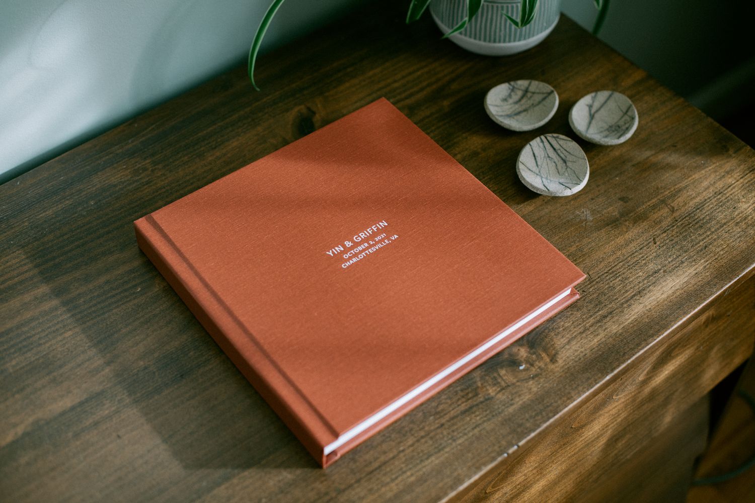 Elegant terra cotta colored wedding album book on wooden table with decorative elements.