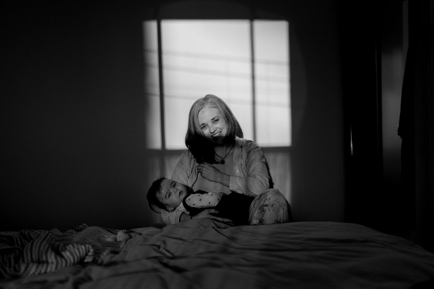 Black and white photo showing someone reading by window light while sitting on a bed.