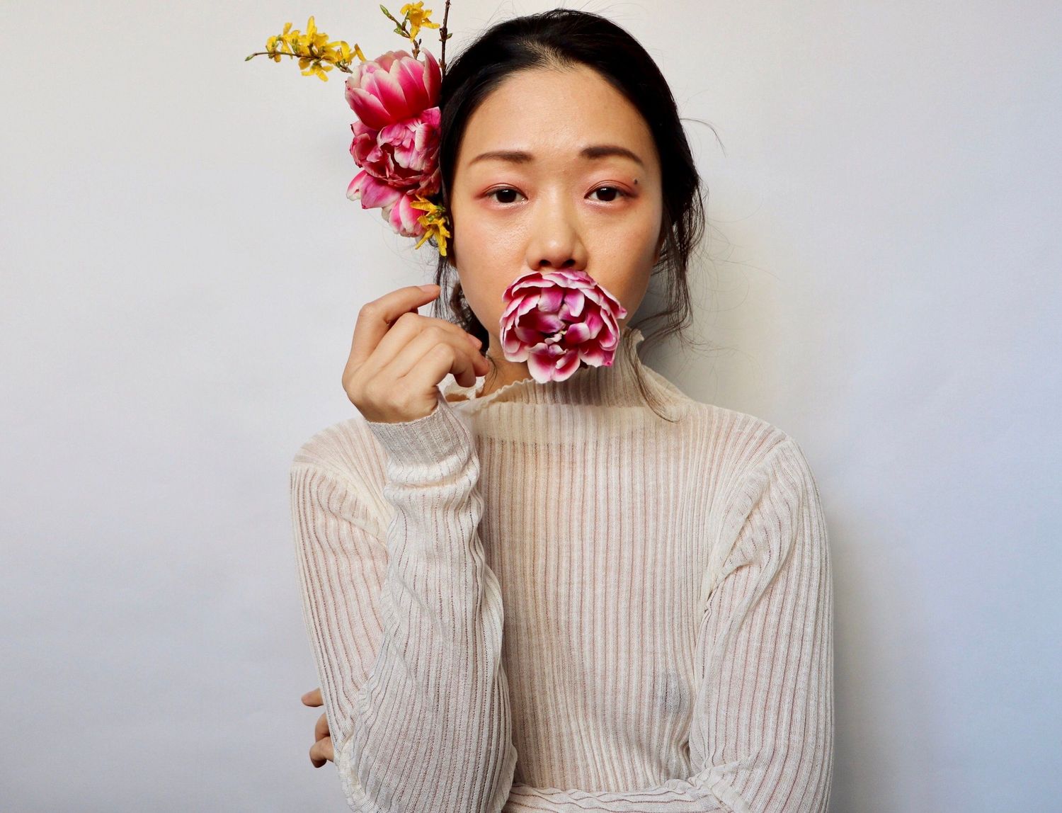 Person in cream sweater poses with pink flowers against white background.