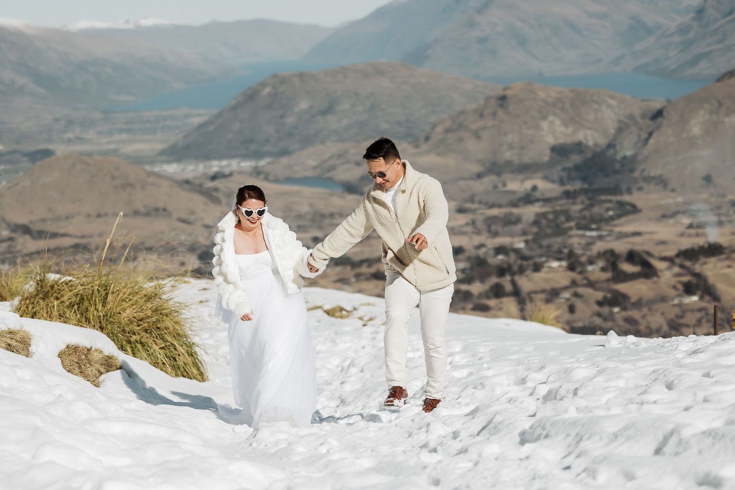A wedding photoshoot in a snowy mountain landscape with dramatic peaks and valleys in the background.