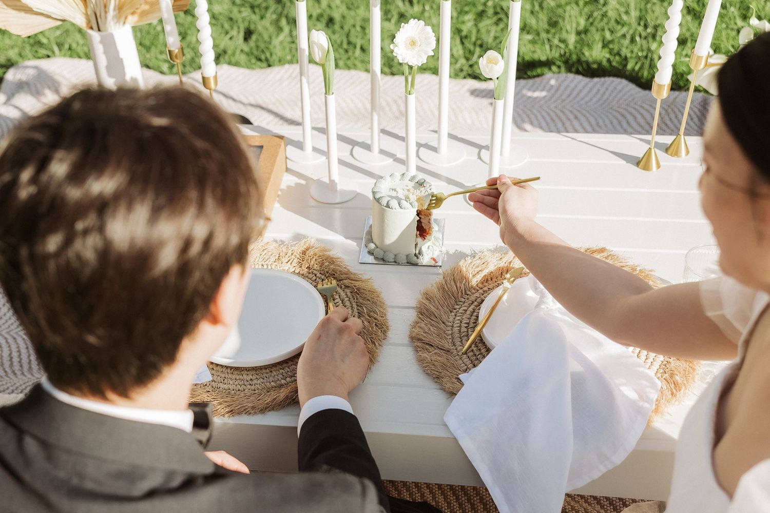 Person reaching up to adjust decorative white hanging ribbons at an outdoor wedding venue.