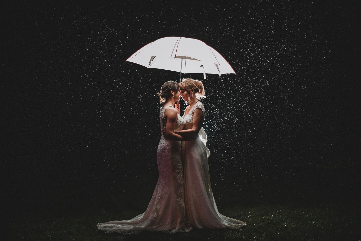Artistic rainy night wedding portrait under a white umbrella with dramatic lighting.