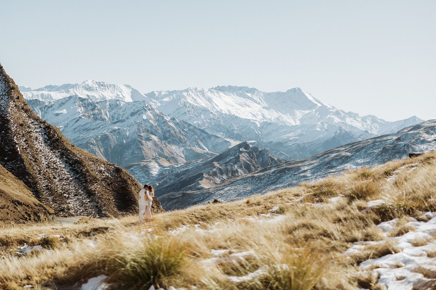Snow-capped mountain peaks rise above golden grass in a scenic alpine landscape.