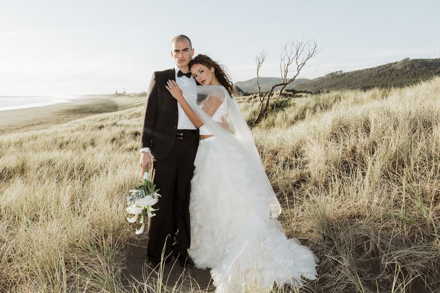 A romantic wedding photoshoot in a scenic field with tall grass and natural lighting.