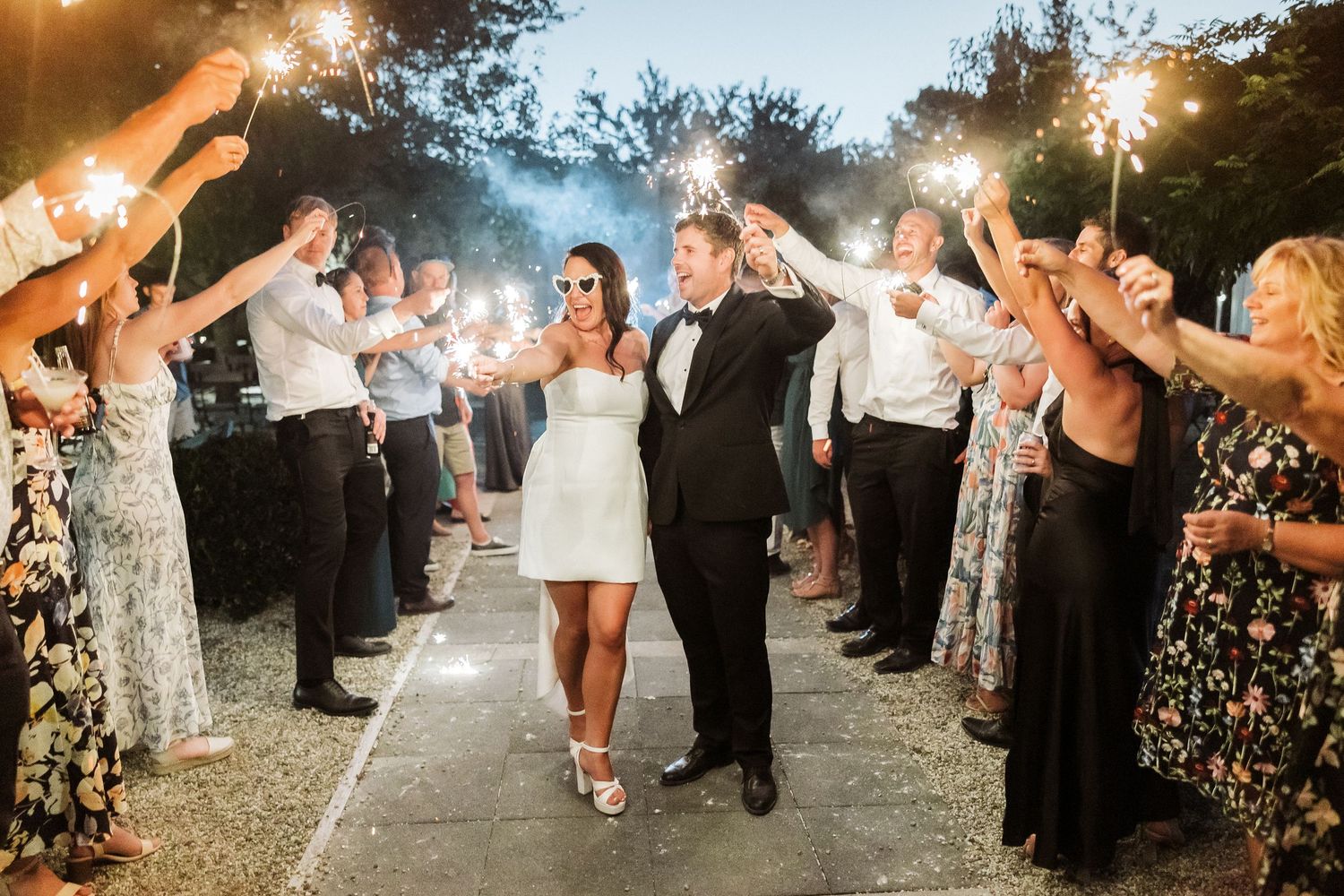Wedding guests hold sparklers creating a magical light tunnel as newlyweds dance through during evening celebration.
