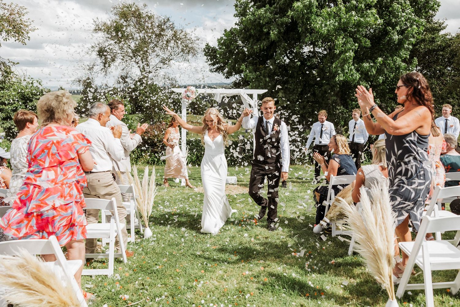 Wedding guests celebrate with bubbles during an outdoor summer garden ceremony.