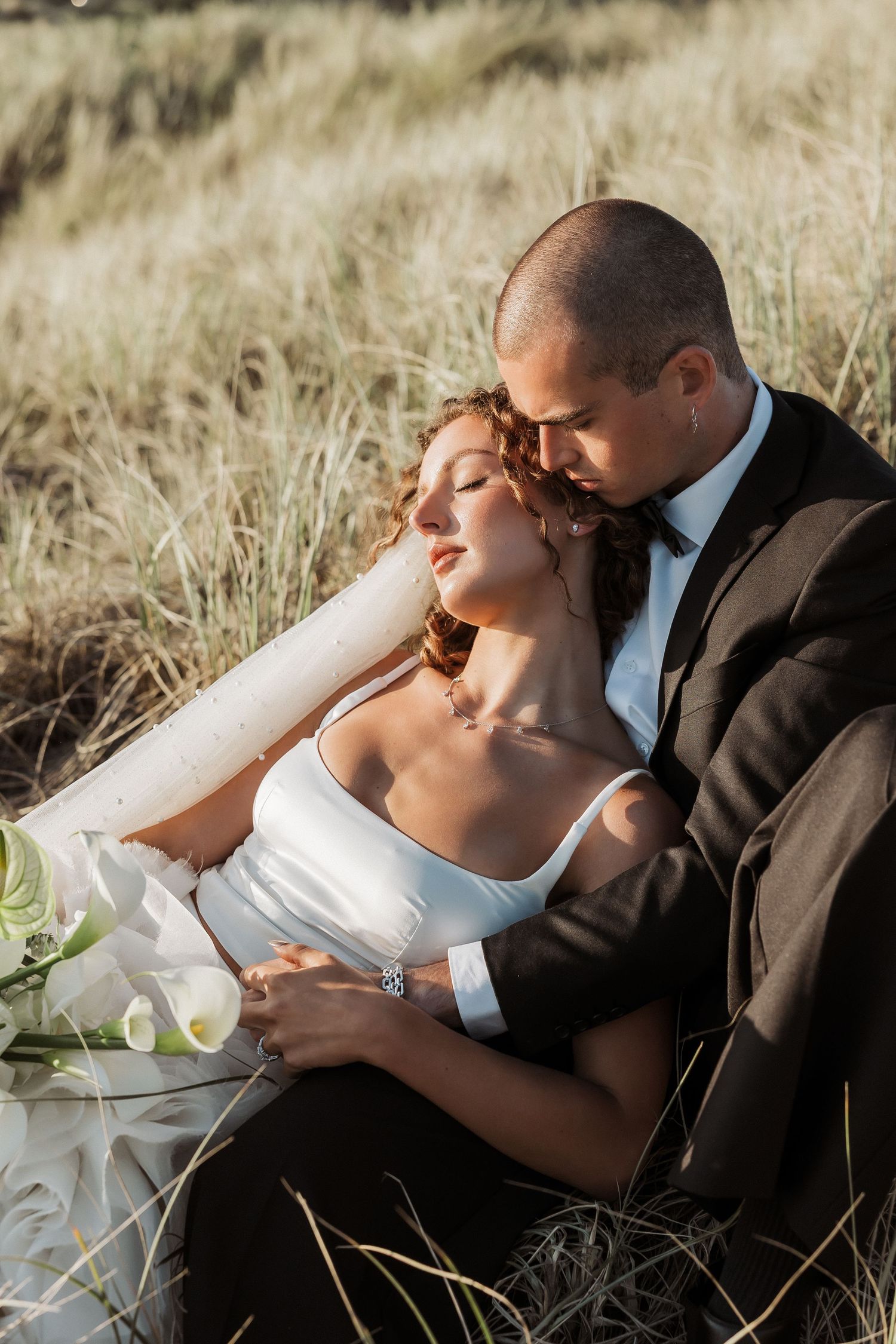 Intimate wedding portraits of newlyweds laying in golden grass field.
