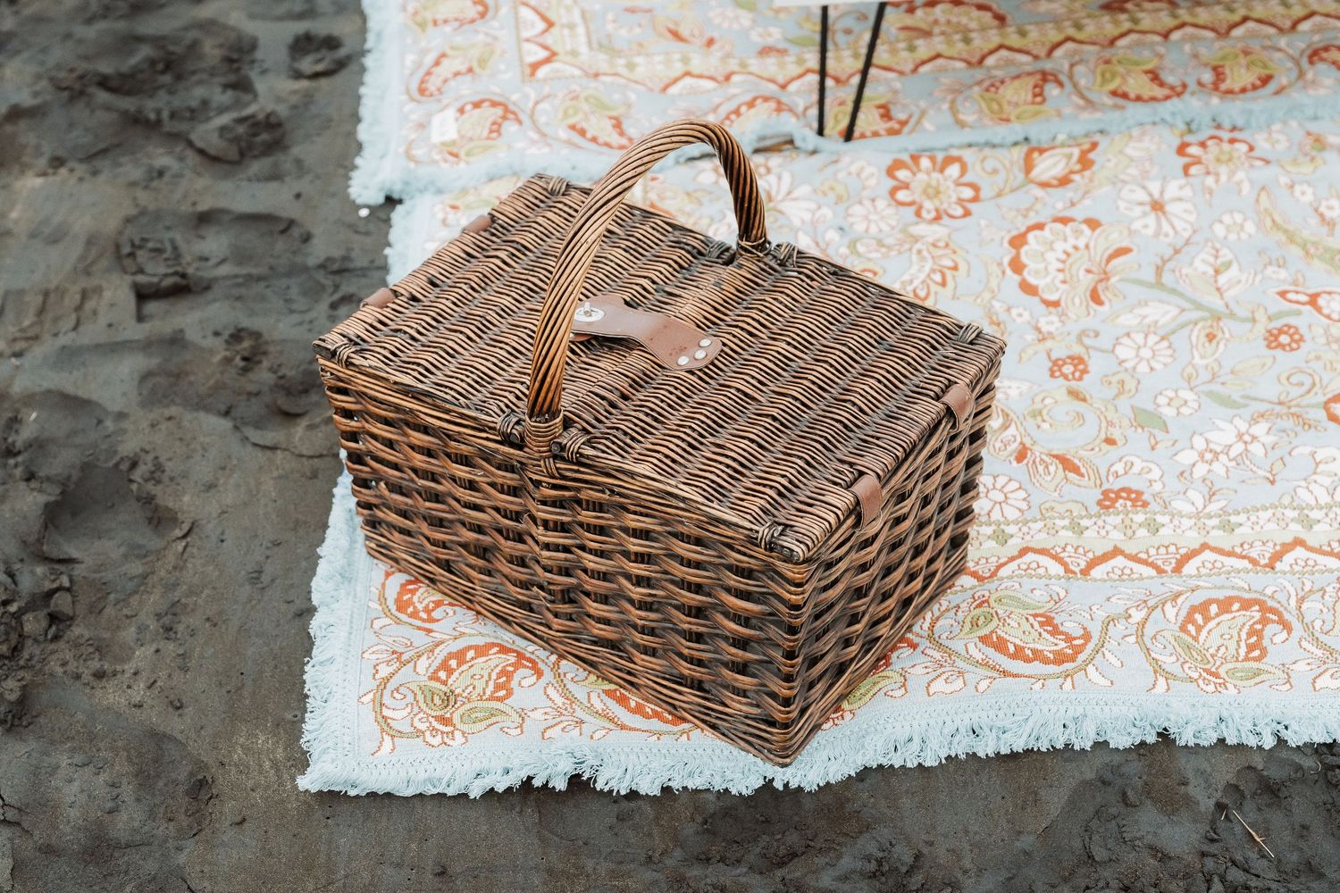 A woven picnic basket sits on a decorative tablecloth with delicate orange floral patterns.