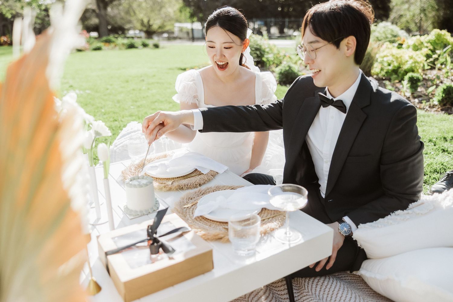 Couple sharing a sweet moment while cutting their white wedding cake at an outdoor reception.