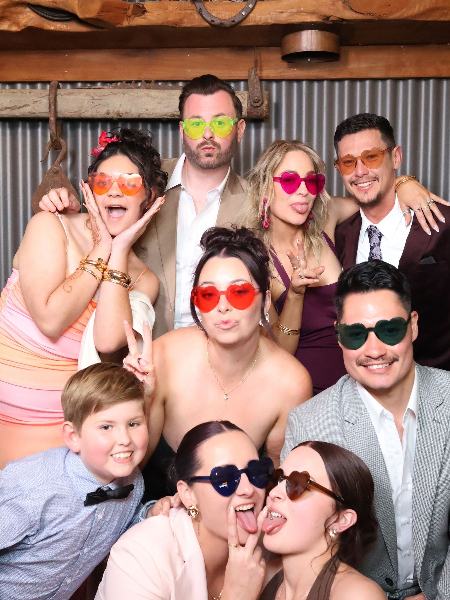 Group wearing colorful sunglasses poses together at a photo booth party with fun and playful expressions.