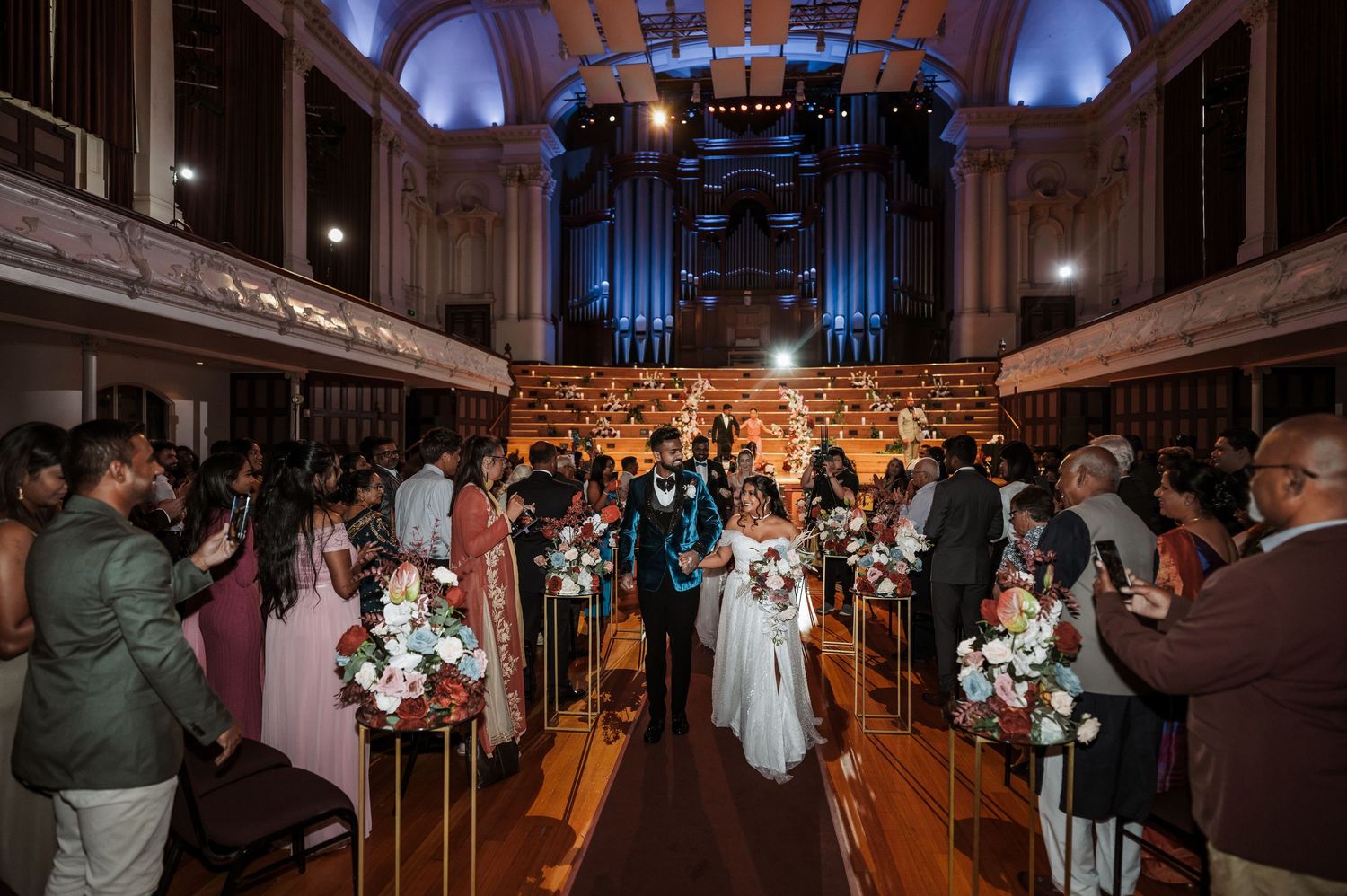 Wedding guests dance on an illuminated ballroom floor during an evening reception at an elegant venue.