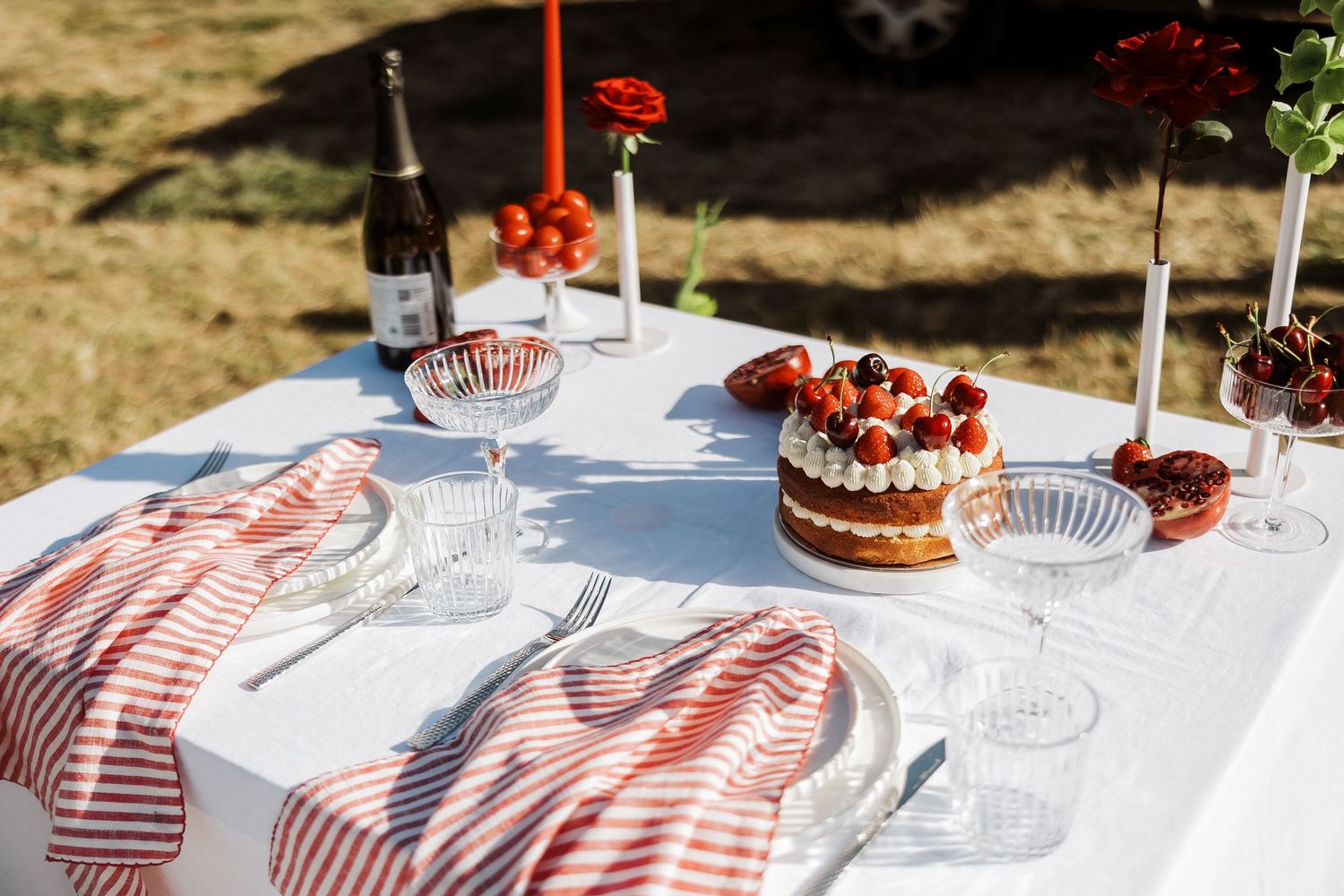 Wedding reception table decorated with red floral centerpieces and white candles on a light blue tablecloth.