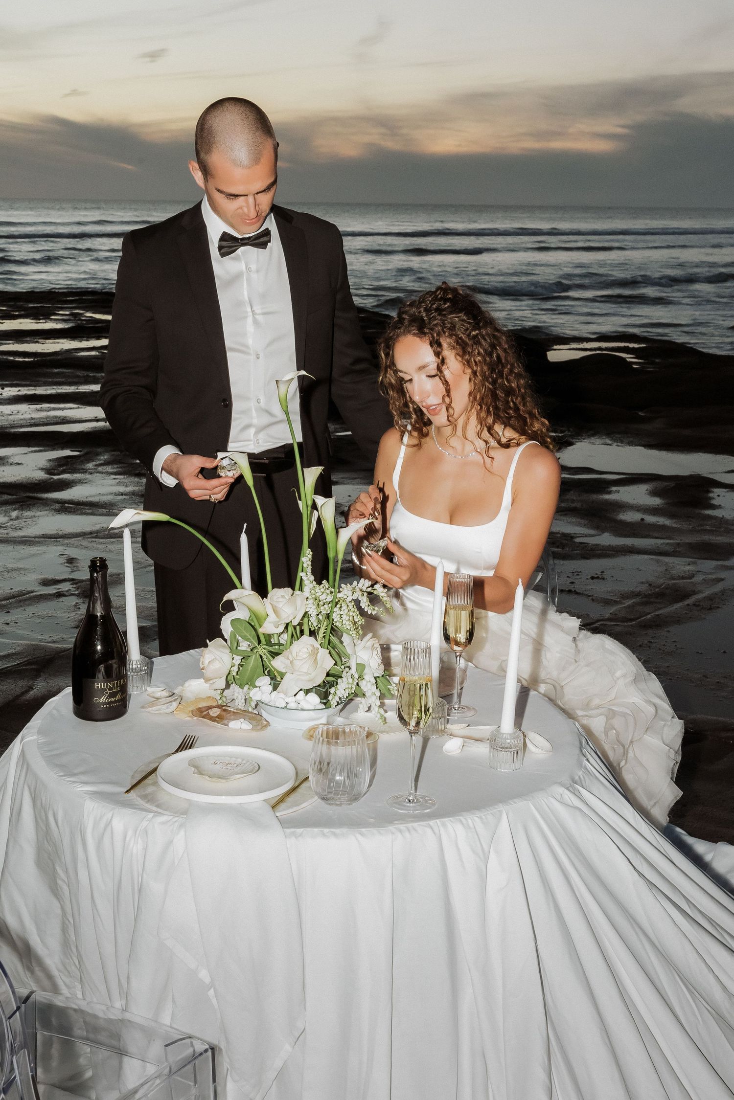 Elegant beachside dinner setup with white tablecloth and place settings at sunset.