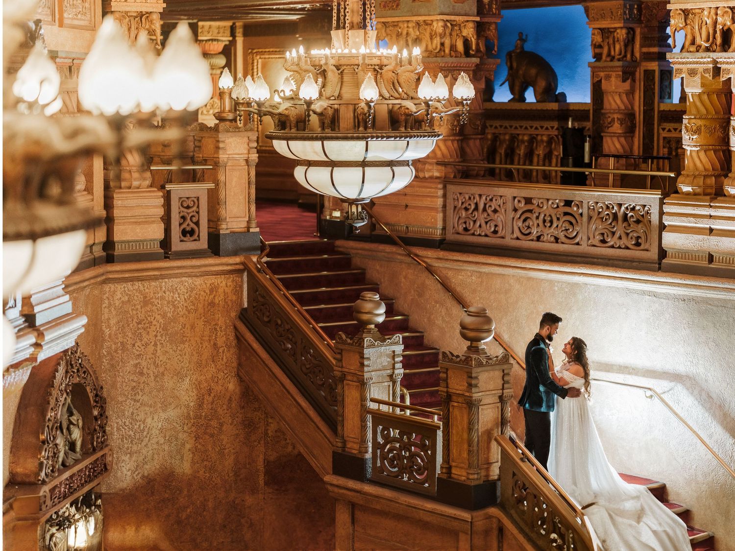 Ornate vintage staircase with carved wooden details and elegant lighting fixtures in a historic building.