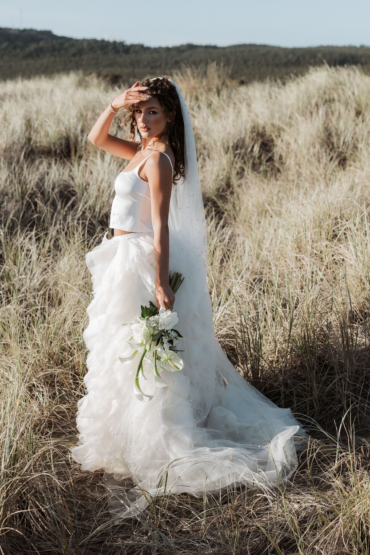 A flowing white wedding dress against golden dried grass in a scenic outdoor setting.