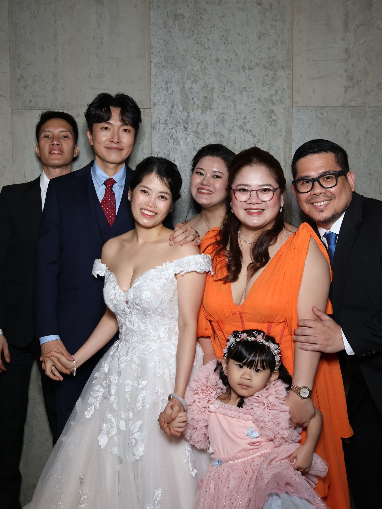 Group photo at formal event with people wearing white, orange, and pink dresses standing together indoors.