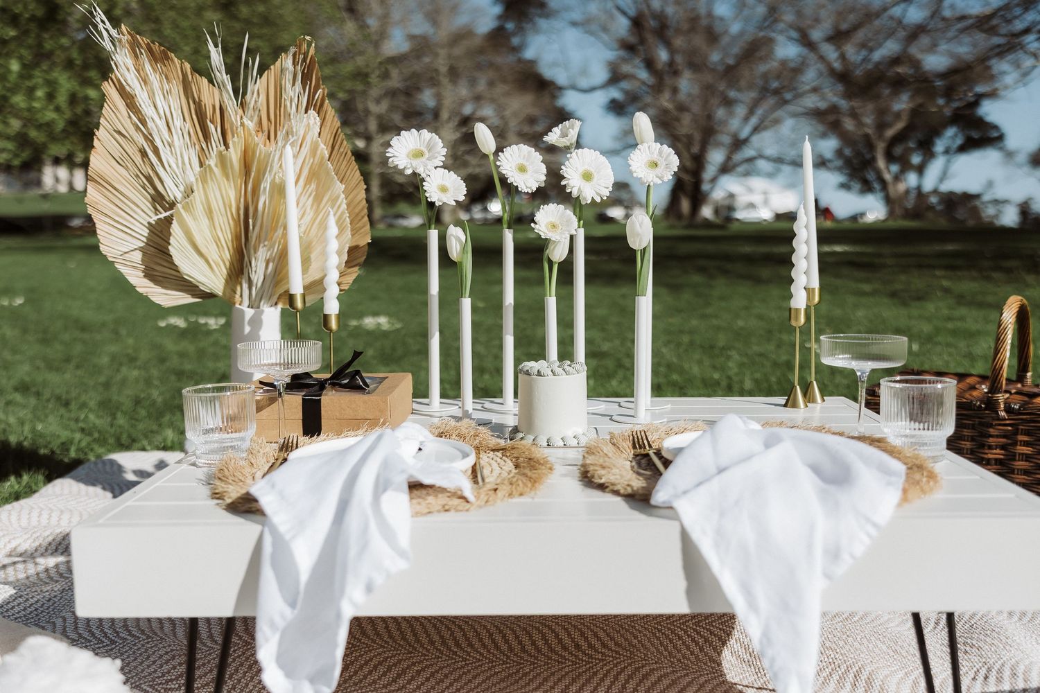 Elegant outdoor wedding reception table settings with white linens, floral centerpieces and taper candles in glass holders.