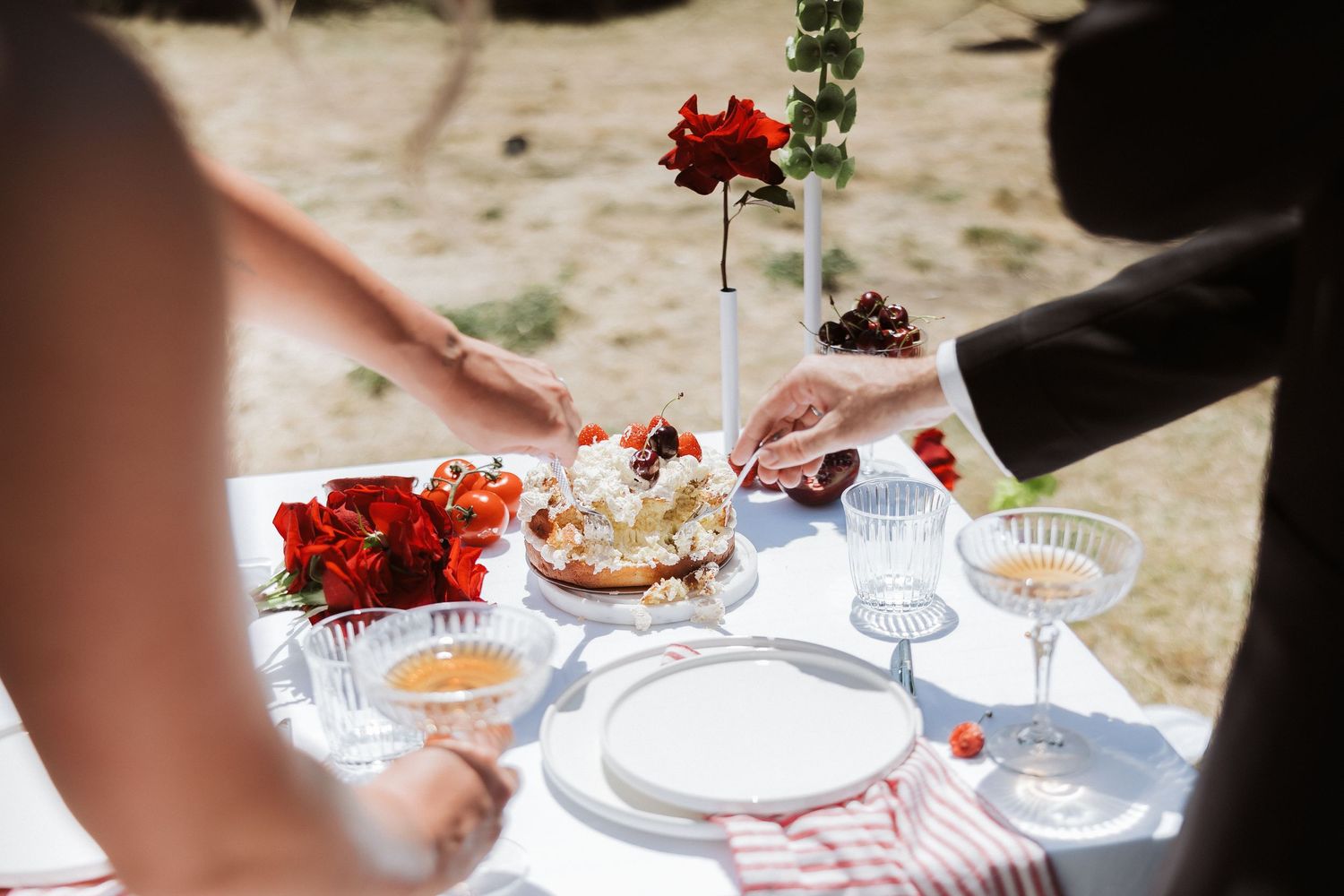 Close-up of table settings with red roses and elegant dishware at an outdoor vineyard event.