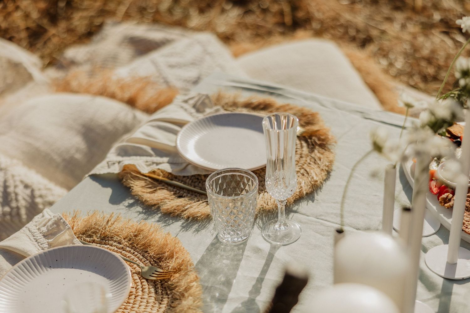 A rustic table setting with dried wheat stalks, white plates, and crystal glassware arranged for an elegant dinner party.