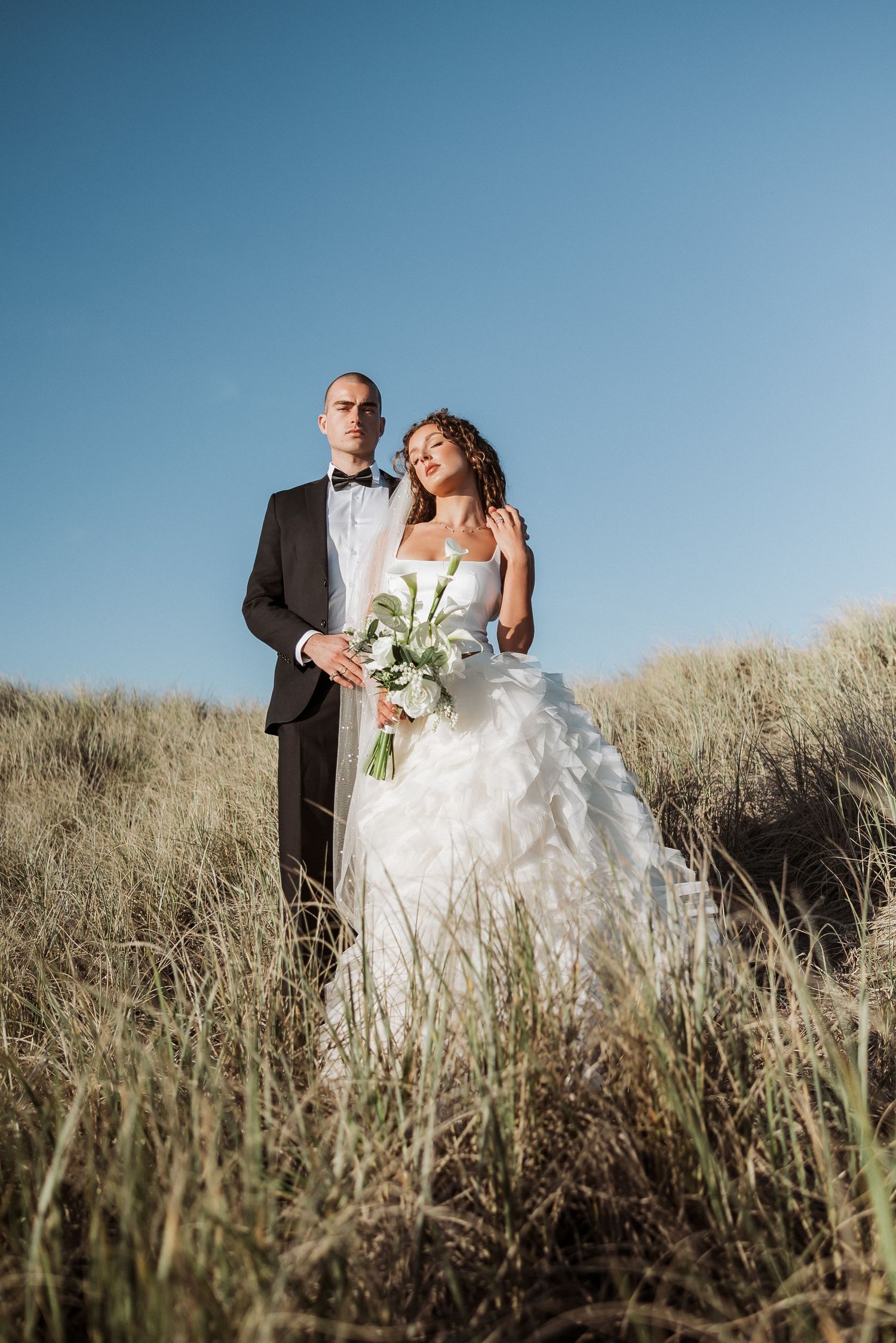 Newlywed couple embracing in tall grass on a hillside during golden hour wedding photoshoot.