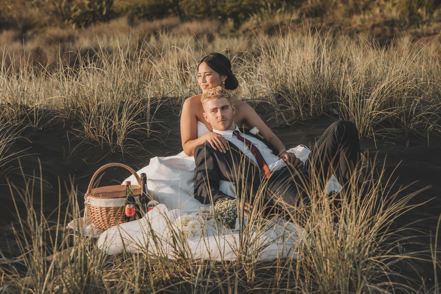 A romantic wedding photoshoot in tall grass at sunset with warm golden lighting.