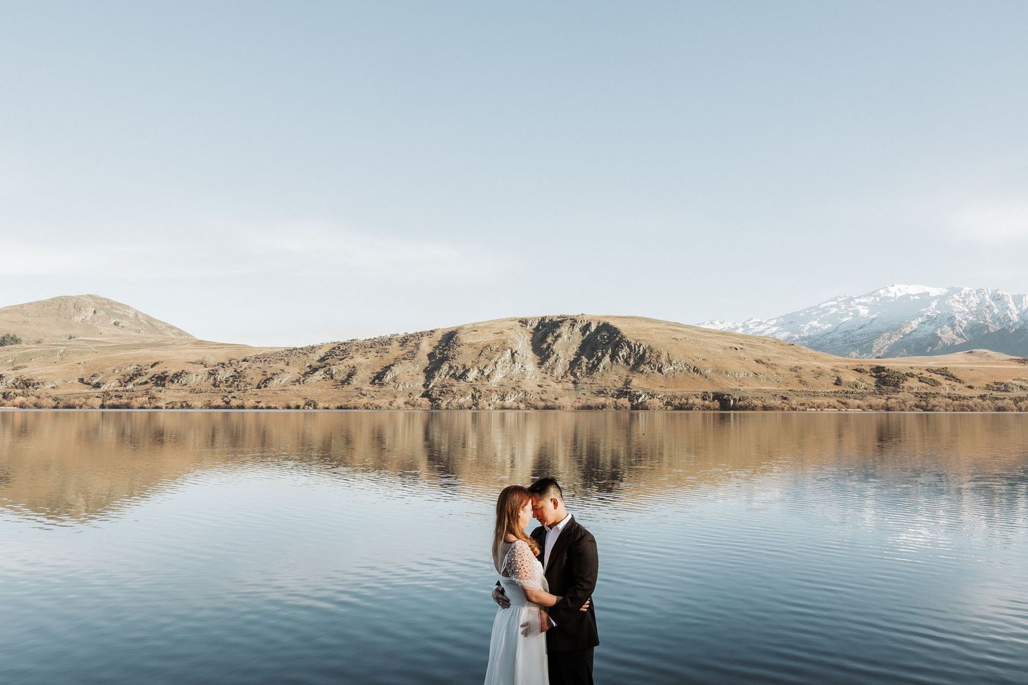 Snow-capped mountains reflect in a serene alpine lake surrounded by rugged terrain in New Zealand.