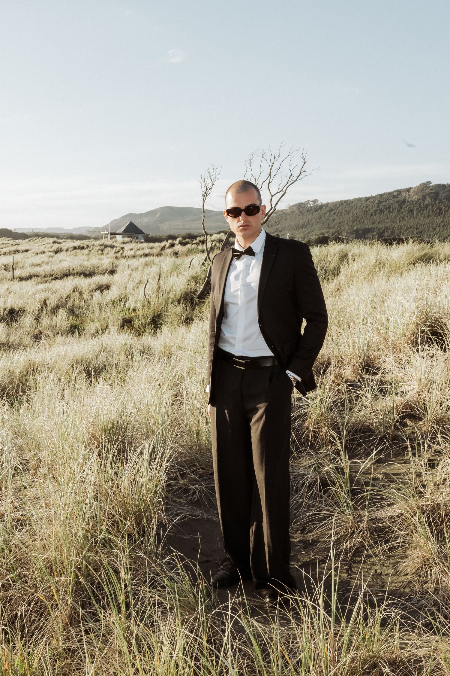 Formal wedding attire photographed in a rustic field with dried grass and mountains.