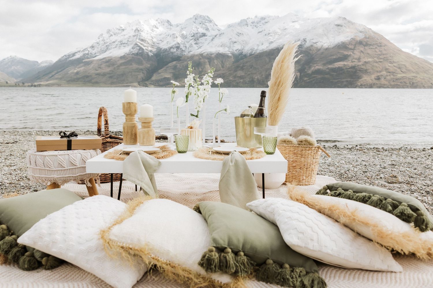 Elegant beige and white coastal wedding table settings with floral arrangements and linens against a mountain backdrop.
