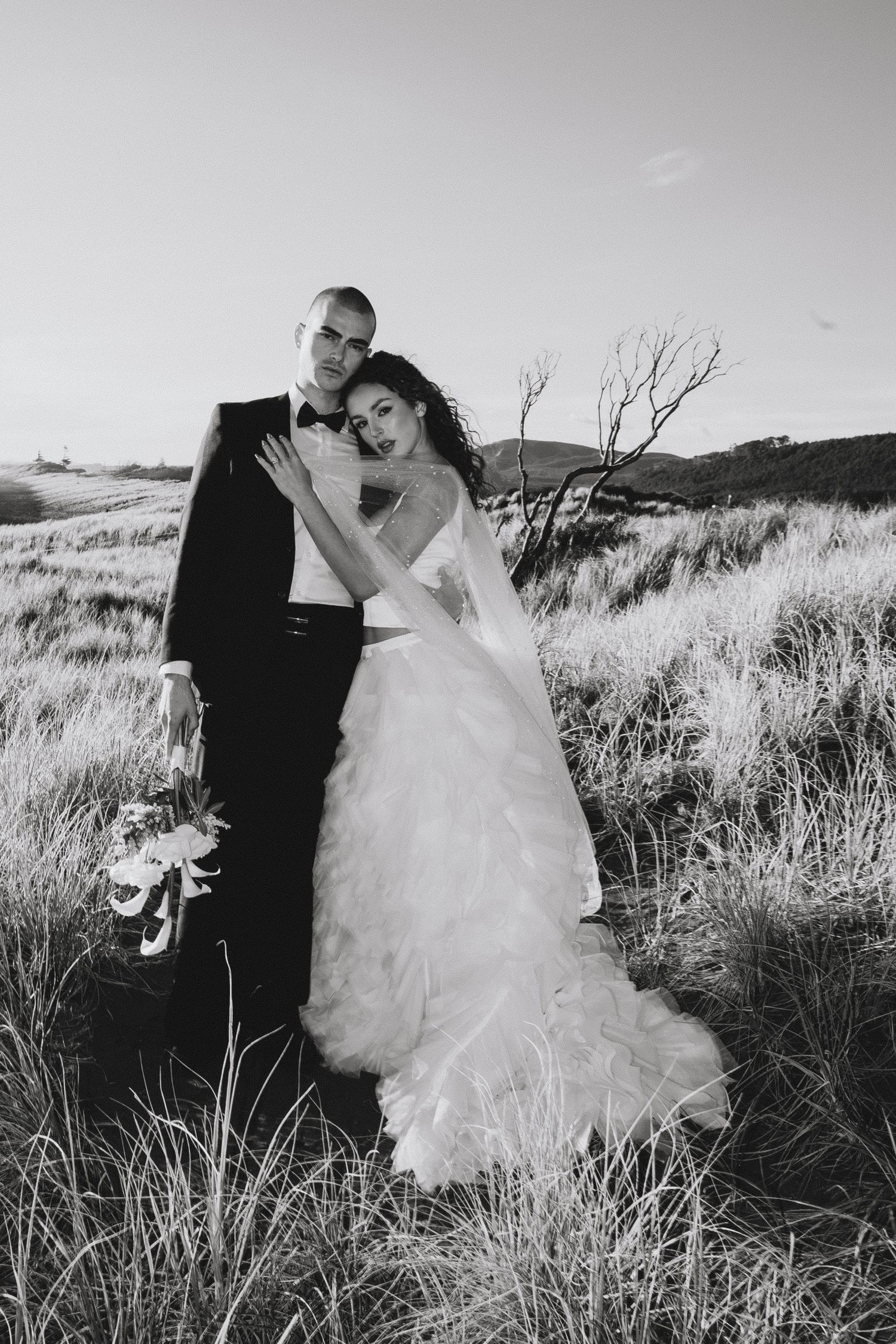 Black and white wedding photos show a couple embracing in tall grass on a hillside.