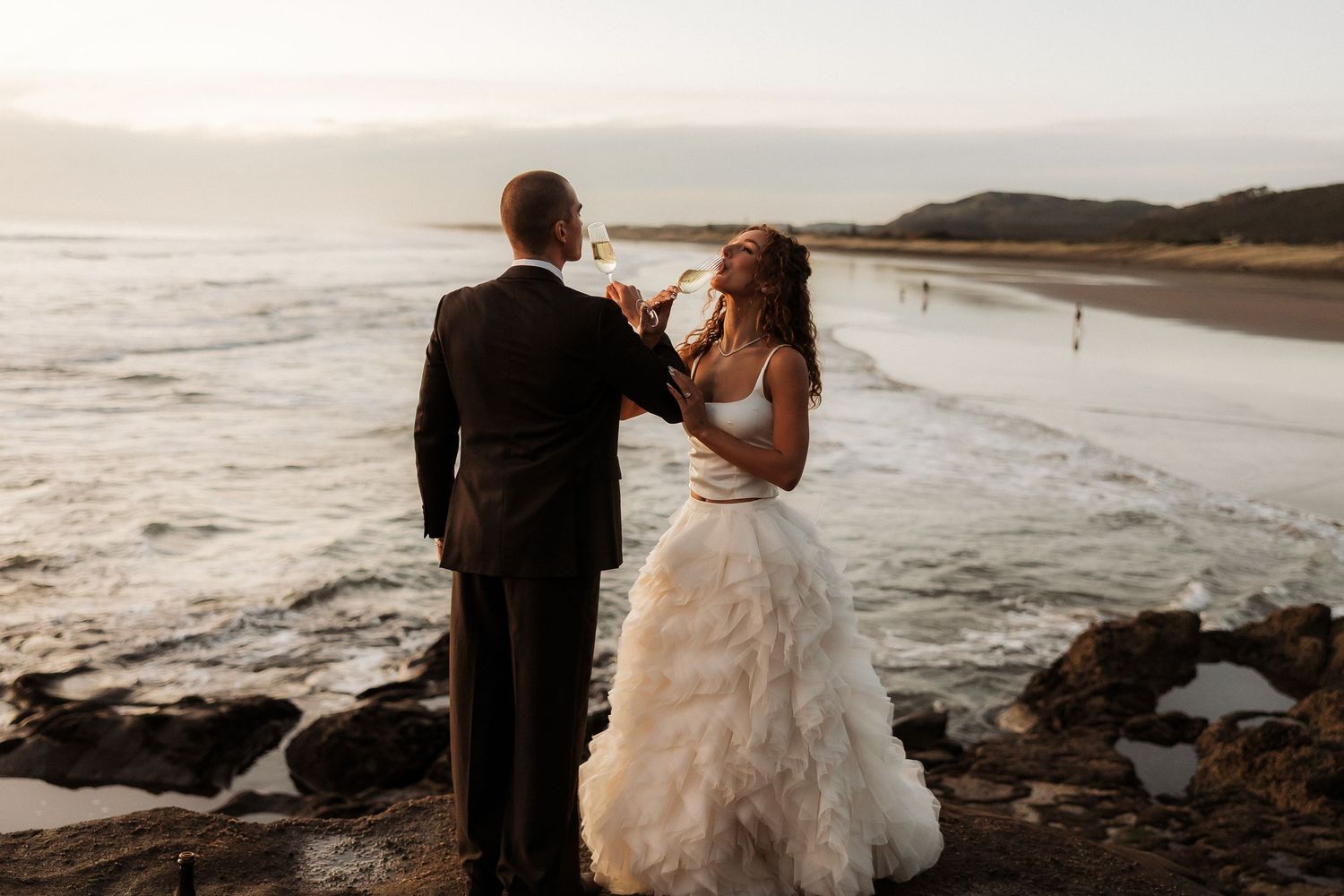 Couple sharing an intimate moment on rocky beach during sunset wedding celebration.