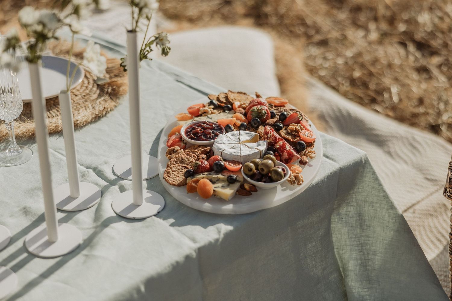 Elegant table setting with rustic plates, glasses and floral arrangements in warm sunlight creating long shadows.