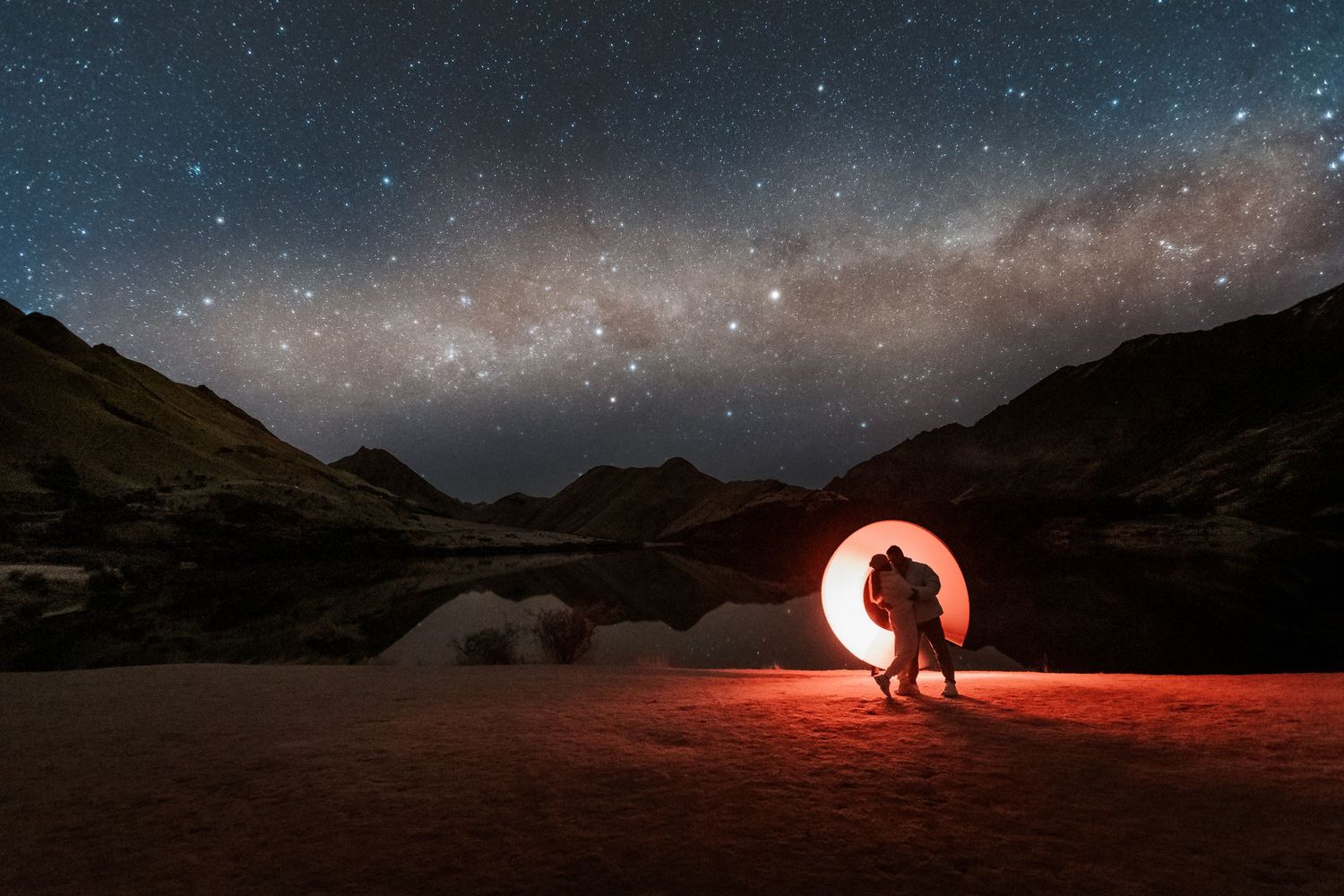 Stunning starlit night sky over mountainous landscape with red light painting creating dramatic long exposure effects.