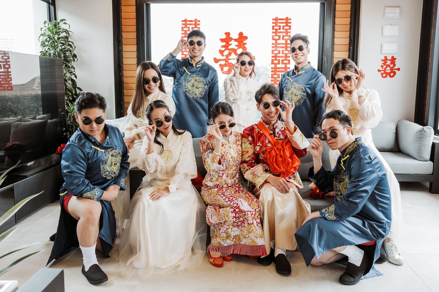Traditional Chinese wedding ceremony with bride in red qipao and groom in blue suit sitting together in modern venue.