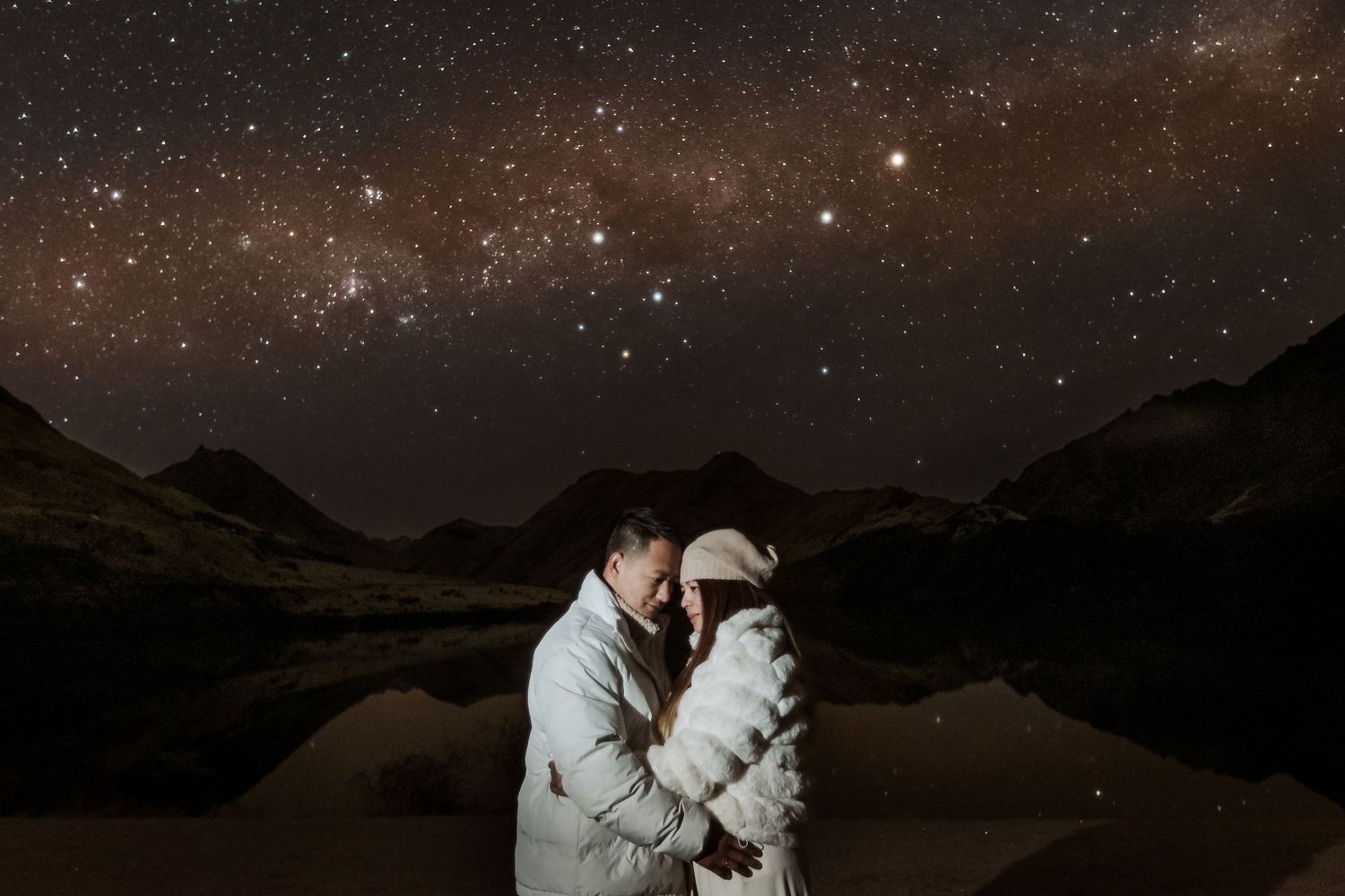Couple embraces under a starry night sky in the mountains with dramatic lighting and silhouettes.